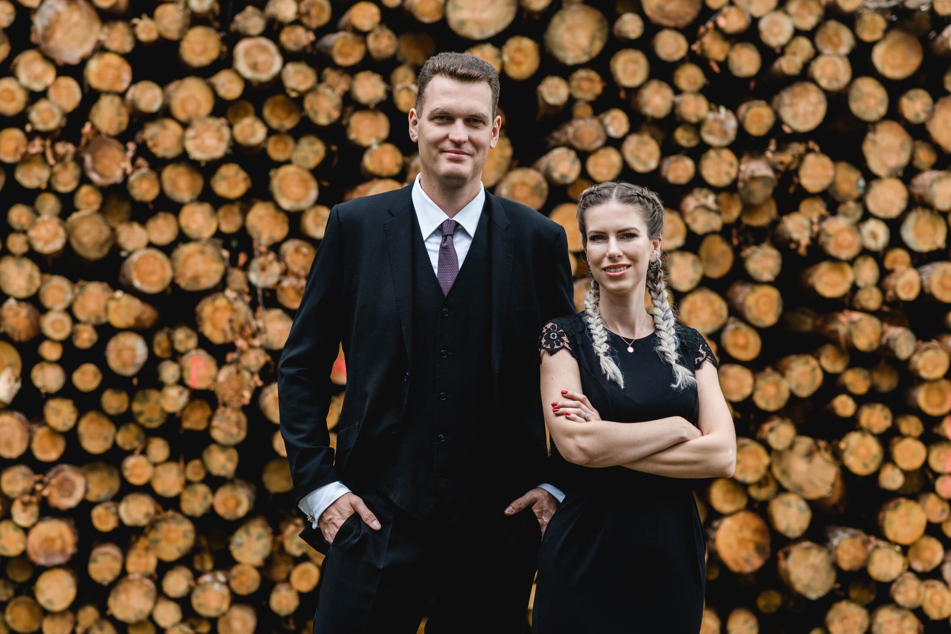Frau und Mann stehen vor einem Stapel Holzstämme