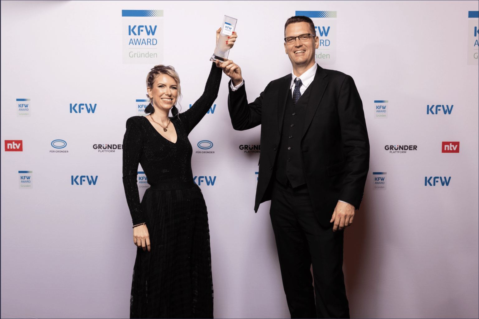 Preisverleihung KfW Award Gründen: Frau und Mann halten die Trophäe vor der KfW-Logowand
