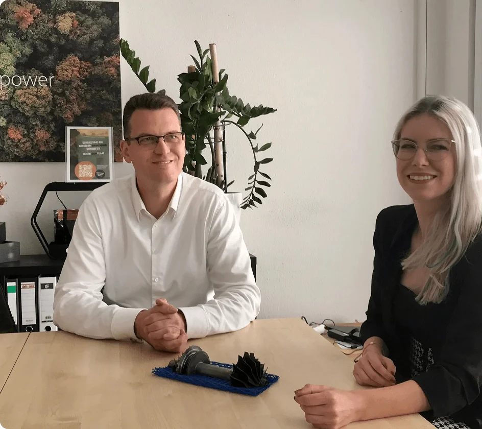 Zwei Personen sitzen an einem Besprechungstisch, vor ihnen ein Turbinenmodell